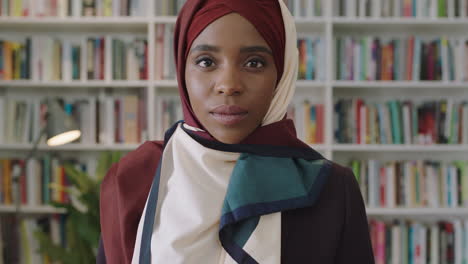 Retrato-De-Una-Joven-Y-Encantadora-Mujer-Afroamericana-Mirando-A-La-Cámara-Estudiante-Parada-En-La-Biblioteca