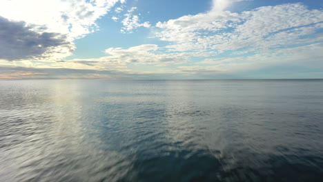 AERIAL:-Flying-Very-Low-Above-the-Surface-of-Sea-into-the-Horizon-with-Blue-Cloudy-Sky