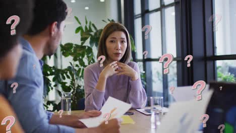 Animation-of-question-marks-over-diverse-business-people-having-meeting-at-office