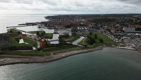 Lancha-Motora-Navegando-Por-El-Mar,-Enorme-Castillo-Directamente-En-La-Costa,-Ranura-De-Kronborg,-Pequeño-Puerto-Con-Muchos-Barcos-En-El-Mar,-Mar-Báltico,-Helsingor,-Dinamarca,-Europa,-Drone