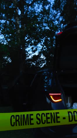 vertically filmed video of a yellow colored crime scene do not enter police tape ribbon pulled in front of a black sedane car or vehicle at night while its indicator lights are blinking, opened doors
