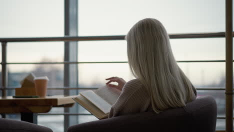 ack view of high school student preparing for exam, focused and flipping to a new page in textbook while sitting in a quiet study space, with natural light coming through the window