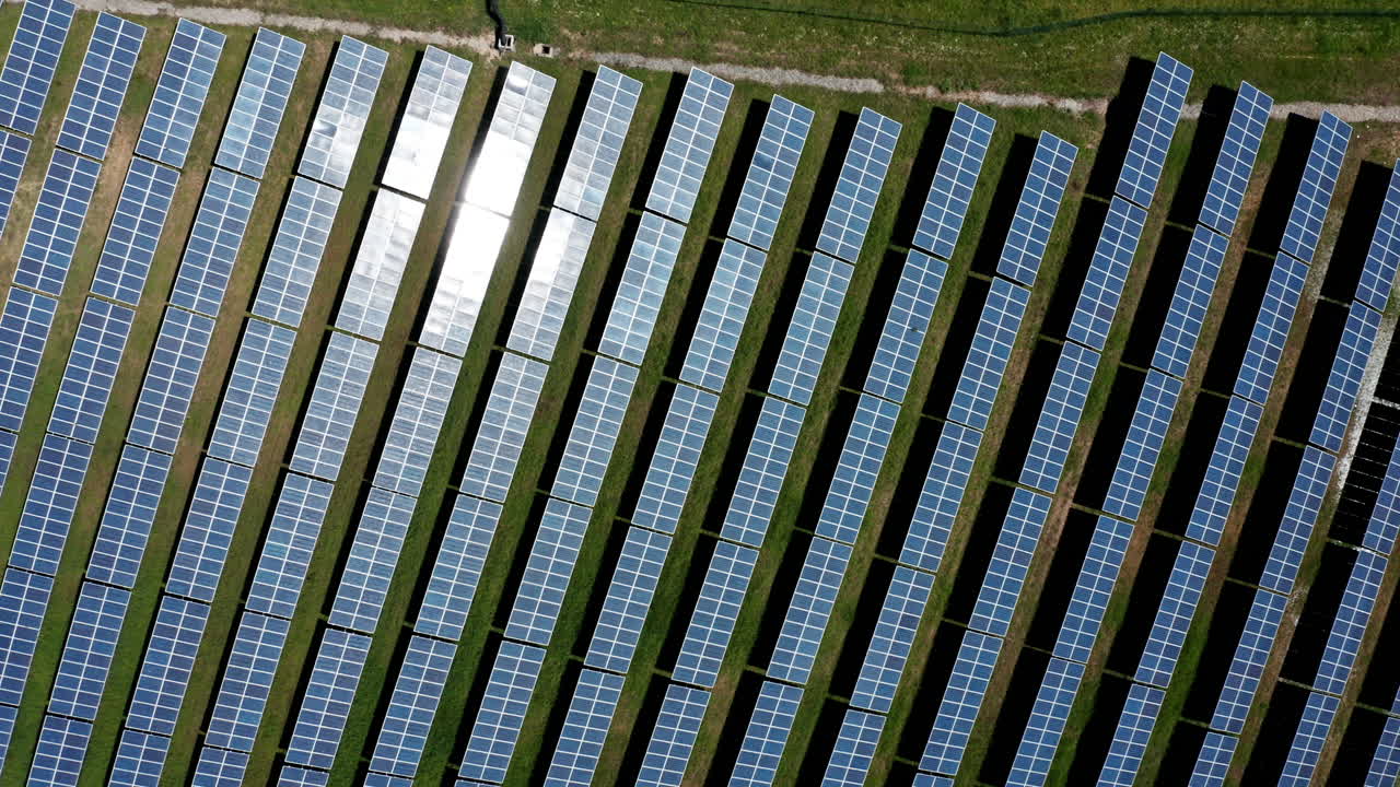 Rows of solar panels in a green field captured from above on a sunny day
