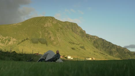 young, blonde, longhaired, caucasian male solo camping in front og scenic mountain in sunrise