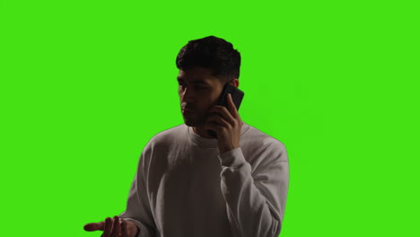joven hablando en el teléfono móvil de pie contra el fondo del estudio de pantalla verde con iluminación de baja clave 2