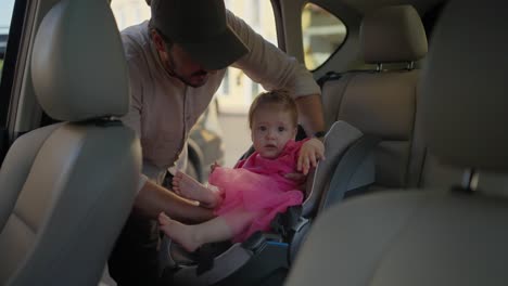 father buckles his baby girl into a car seat