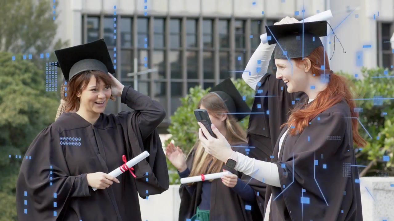 Kızıl saçlı mezun telefonunu gösteriyor, kepinin üzerinde diplomasını kaldırıyor; arkadaşları gülerken kampüs mezuniyetini kutluyor.