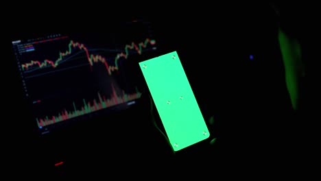 a trader holds a smartphone with a green screen in hands in a dark room. 4k