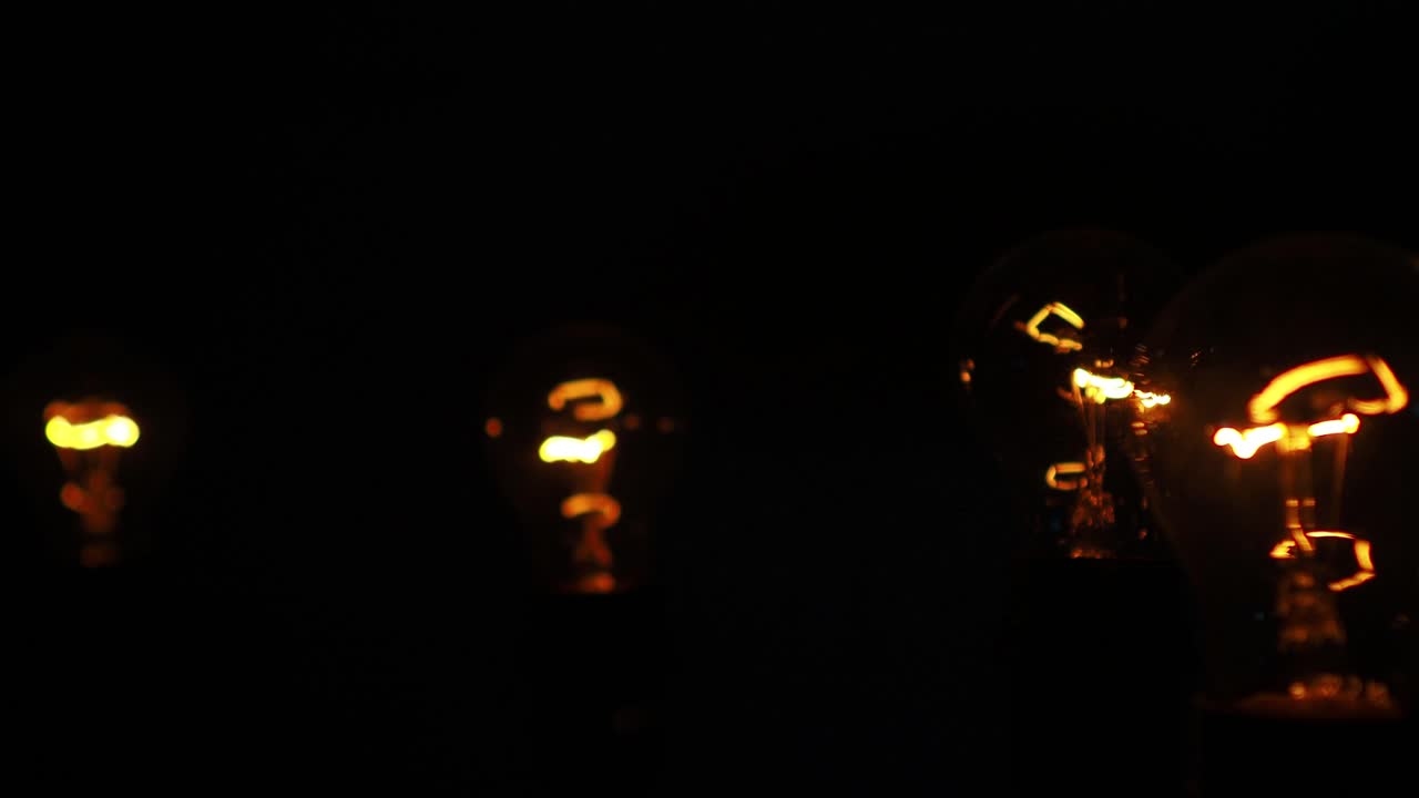 검정색 배경에 빨간색 주황색 텅스텐 필라멘트가 있는 백열 램프, 느린 팬 샷