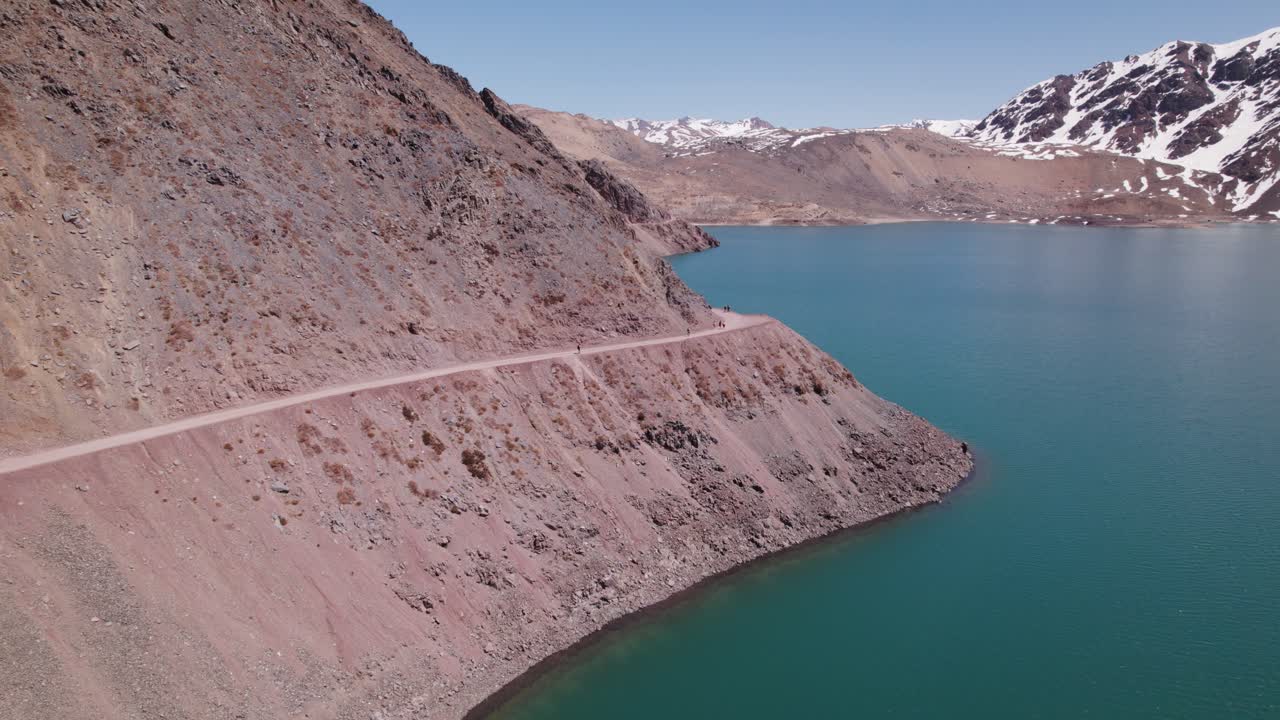 Giornata di sole sopra il bacino idrico El Yeso a Santiago, Cile, con persone che percorrono un sentiero di montagna.