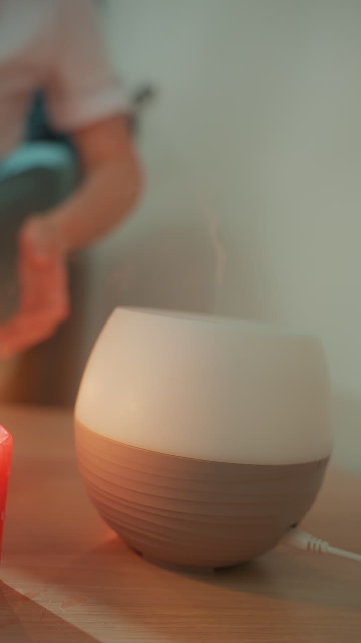 Lampe diffuseur lumineuse et mains ajustant les commandes, lumière d'ambiance de chevet diffusant une chaude lueur ambrée, base en céramique moderne avec cordon, légère pression et rotation pour régler l'illumination, routine du soir pour la relaxation.