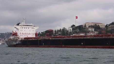 large cargo ship sailing through the bosphorus with istanbul cityscape and turkish flag