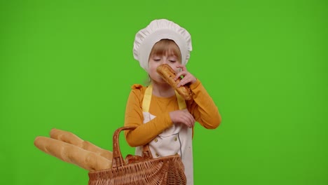 child girl chef showing basket with baguette and bread, smiling, sniffing, eating bun with cream