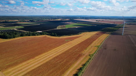 weitwinkelaufnahme aus der luft, die ländliche landschaft mit landwirtschaftlichen feldern, großen solarmodulen und windkraftanlagen an sonnigen tagen zeigt