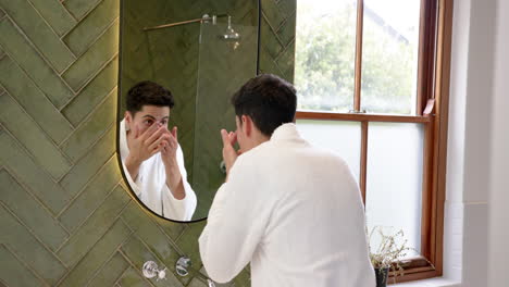 focused biracial man inspecting face in bathroom mirror, slow motion