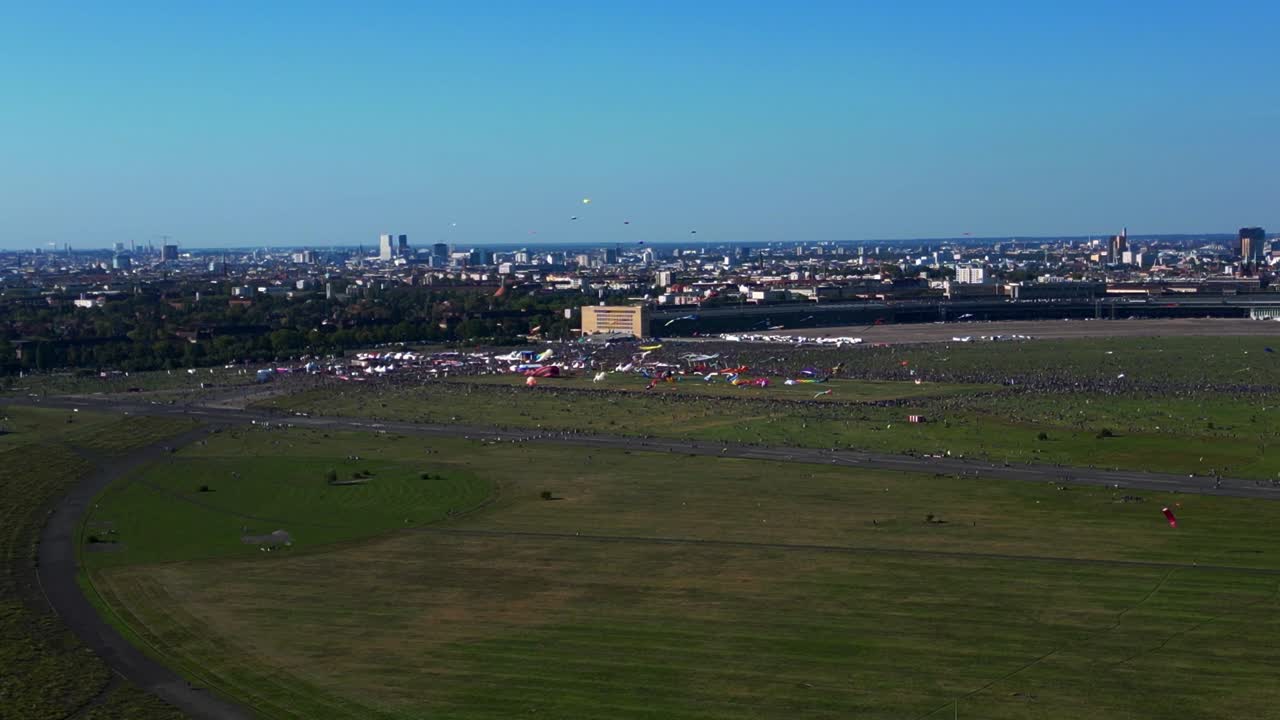 thousands of Berliners enjoying the giant kite festival on a sunny day at Tempelhofer Feld, the former Tempelhof Airport. Smooth aerial view flight panorama overview drone