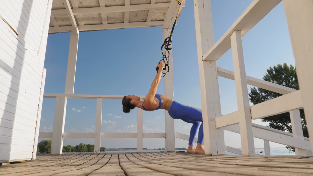 entrenamiento al aire libre. correas de suspensión. entrenamiento con correas. mujer joven atlética está haciendo ejercicios de resistencia de todo el cuerpo usando cuerdas en bucle trx, en la playa durante la puesta o el amanecer. entrenamiento de fitness al aire abierto. concepto de estilo de vida saludable. deporte matutino