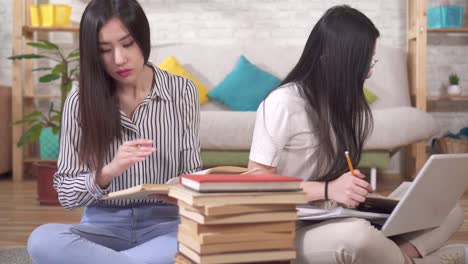 two cute asian students are preparing for the exam sitting on the floor next to books and a laptop in the living room close up