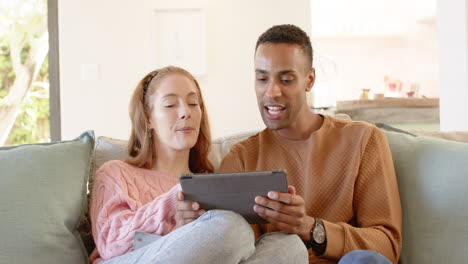 diverse couple relaxing on couch, enjoying tablet together at home