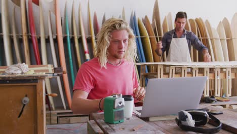 two caucasian male surfboard makers working in their studio and making a wooden surfboard together