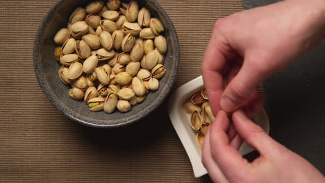 close up shot of person picking up and shelling pistachio nuts from bowl