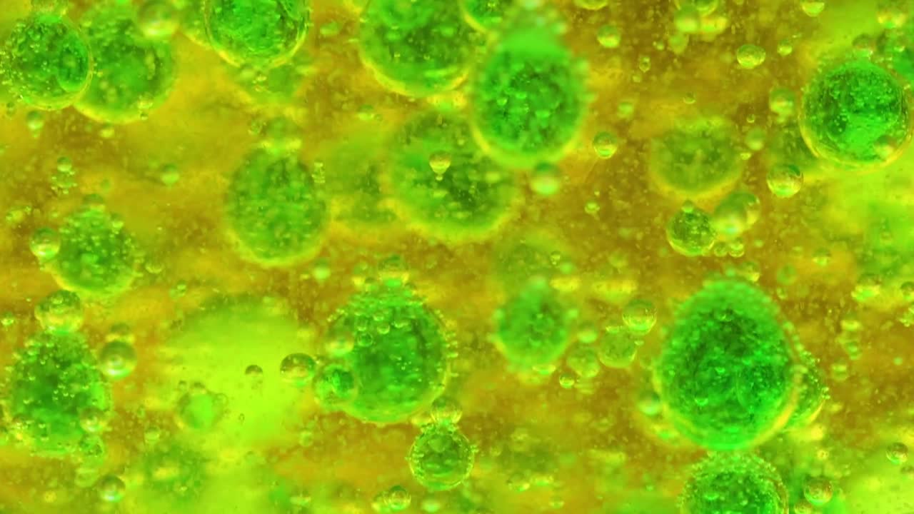 Gotas de aceite de un verde vibrante y burbujas se mueven a través de un fondo de fluido viscoso de color amarillo brillante