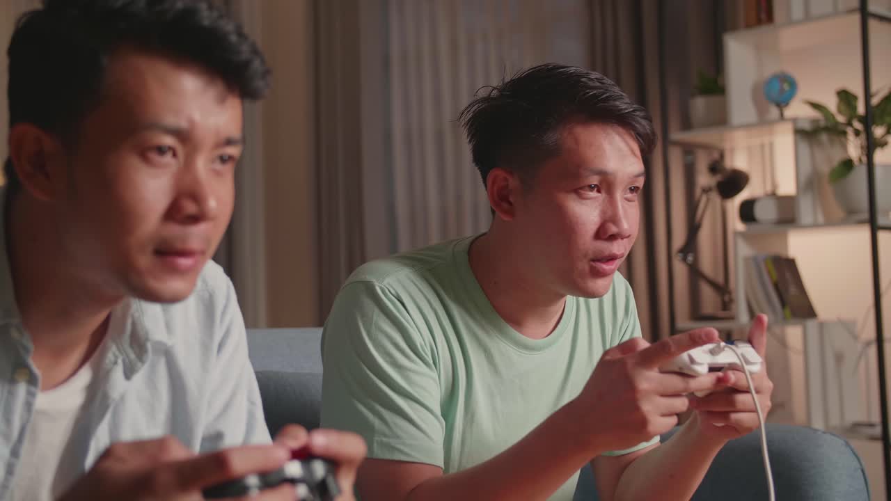 Asian Friends Playing Video Games At Home. Male Happy To Win Victory And Another Man Feeling Disappointed
