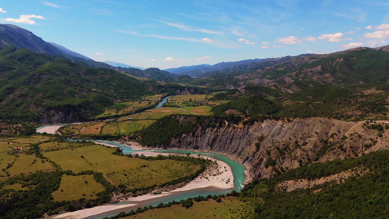 Ripresa aerea sopra campi agricoli e il fiume azzurro brillante nella scenografica valle di Permet, Albania.