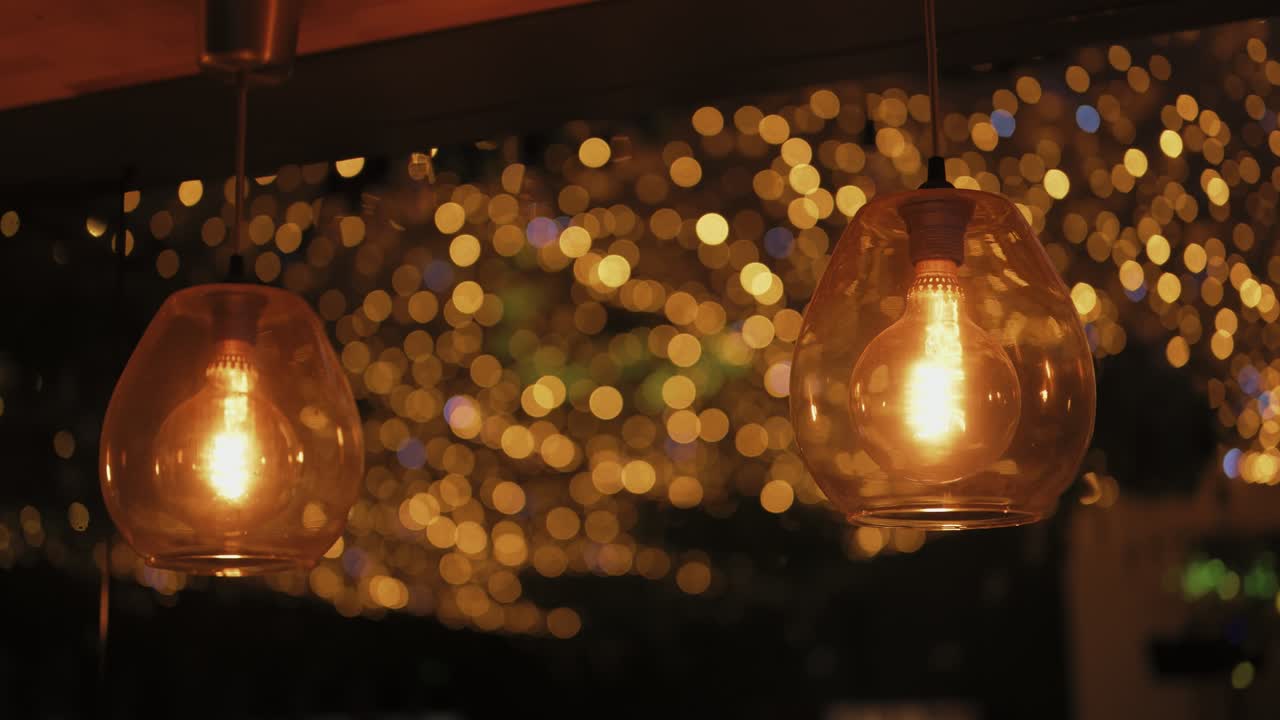 Two glowing pendant bulbs hanging against a blurred background filled with golden bokeh lights creating a cozy, romantic, and festive atmosphere