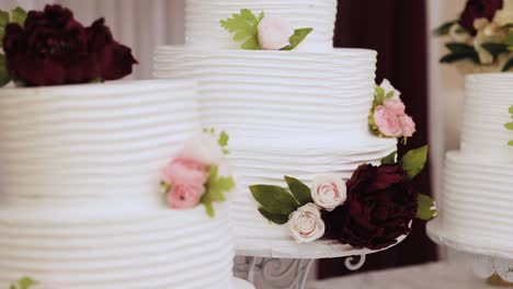 multiple round, layered wedding cakes on a table decorated with white frosting and pink and maroon flowers 1080p 60fps