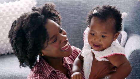 smiling mother cuddling and kissing baby daughter at home