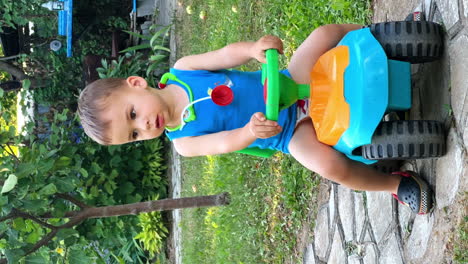 lovely toddler in blue t-shirt and toy stethoscope on his neck sits on toy car. kid lumps up cheerfully and screams. vertical screen.