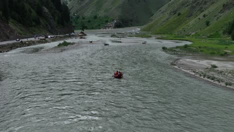 The-drone-glides-over-rafters-navigating-the-vibrant-blue-waters-of-Naran,-with-the-shot-gradually-widening-to-expose-the-breathtaking-scenery-of-towering-mountains