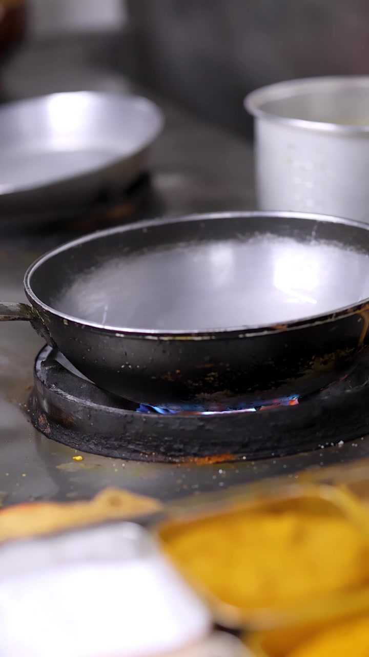 Close-up shot of a black frying pan heating over blue gas flames on stainless steel.