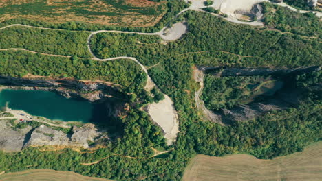 Aerial-footage-of-with-two-old-quarries-with-water-and-winding-paths-near-a-limestone-factory