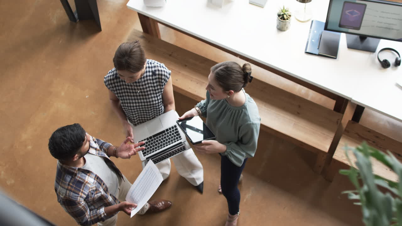 Tre professionisti discutono di lavoro in un ambiente d'ufficio, uno tiene un laptop, un altro dei documenti.