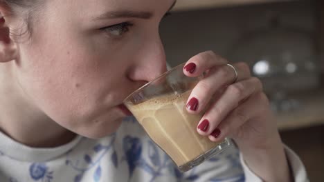 big sip of flat white coffe from a glass, closeup of girl lips and face