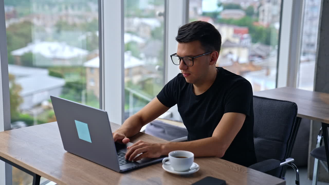 Handsome man freelancer working on computer. Businessman in glasses focused on typing on his laptop. Camera approaches male and he looks straight into camera smiling.