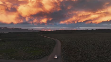 car driving on a dirt road into a wild stormy sunset