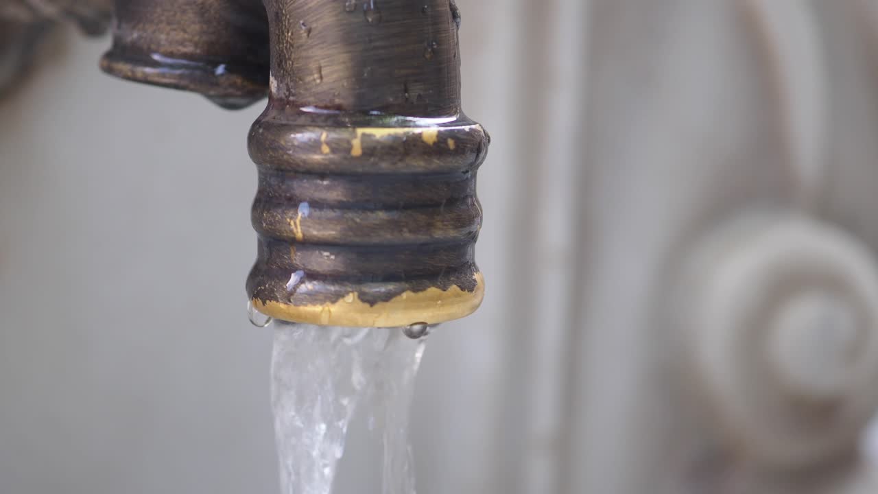 Close-up of Water Flowing from an Old Bronze Faucet
