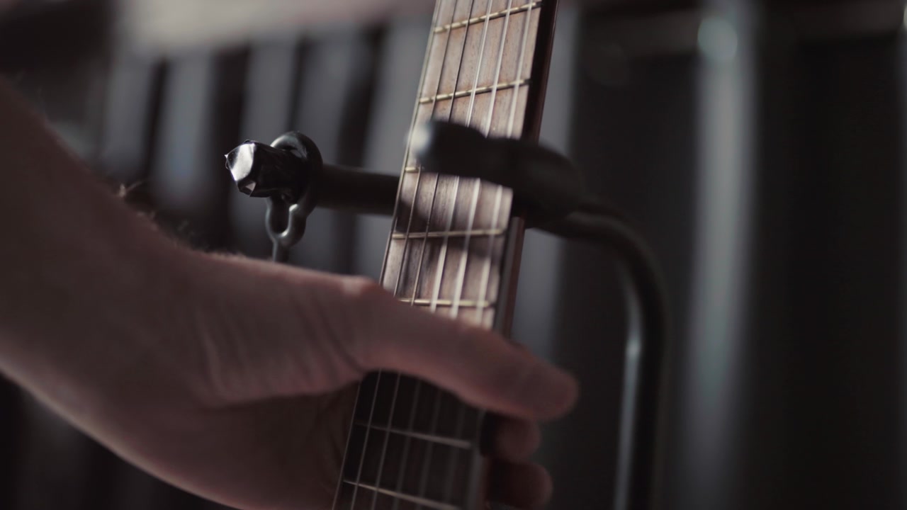Una mano rimuove con attenzione una chitarra acustica da un supporto in una stanza illuminata delicatamente con uno sfondo sfocato.