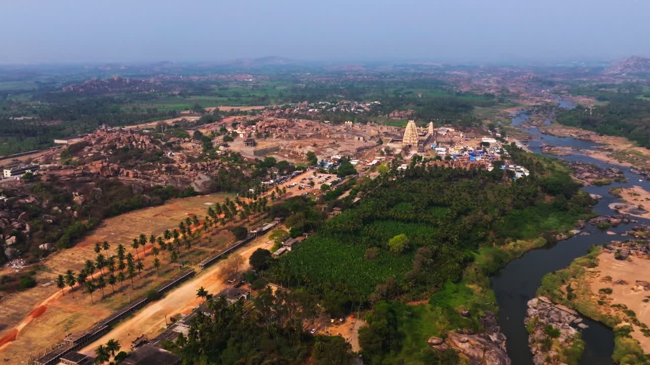 Inquadratura ampia del Tempio di Virupaksha con il fiume Tungabhadra, montagne e campi coltivati a Vijayanagara, Hampi, Karnataka, India. Di giorno, ripresa semi-orbitale, ripresa con drone, 4K.