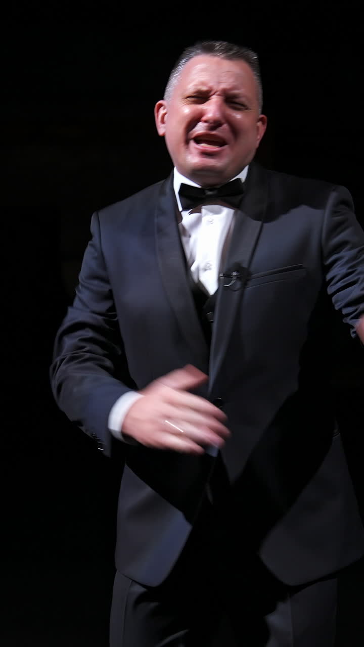 Man is speaking in the light of the floodlights standing on stage to the camera. Actor, artist on performance. Activ gestures with hands. Vertical video