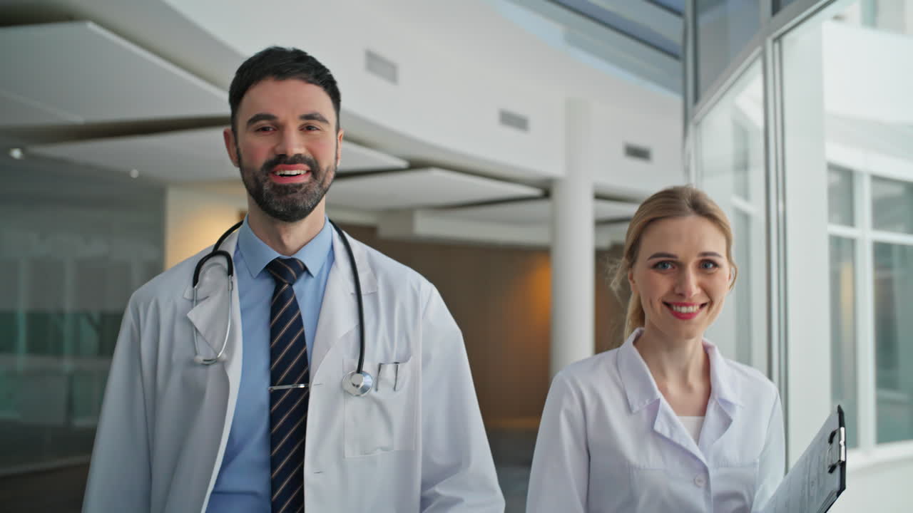 Clinical workers going hallway in white coats. Closeup two doctors look camera