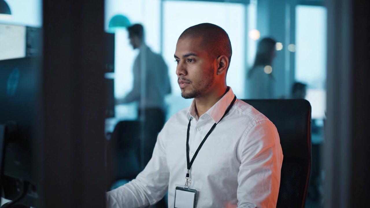 Focused professional in a modern office working on a computer, surrounded by multiple screens, embodying concentration, technology, and corporate environment dynamics.