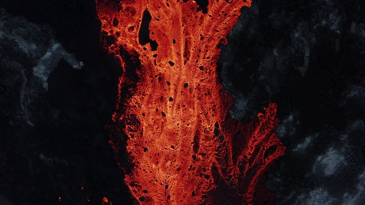 Red burning lava river surrounded by dark basalt rock, top down