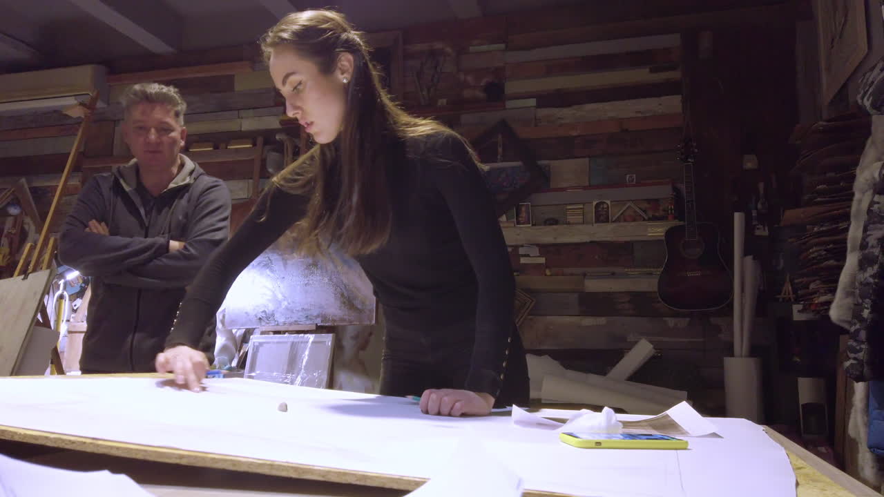Man supervising a woman sketching on a canvas at an art gallery workshop