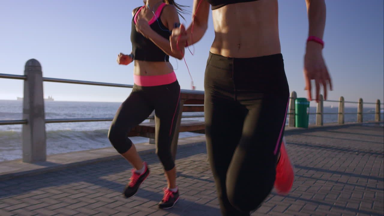 dos mujeres atléticas corriendo al aire libre en cámara lenta en el paseo marítimo al atardecer cerca del océano disfrutando de la carrera nocturna