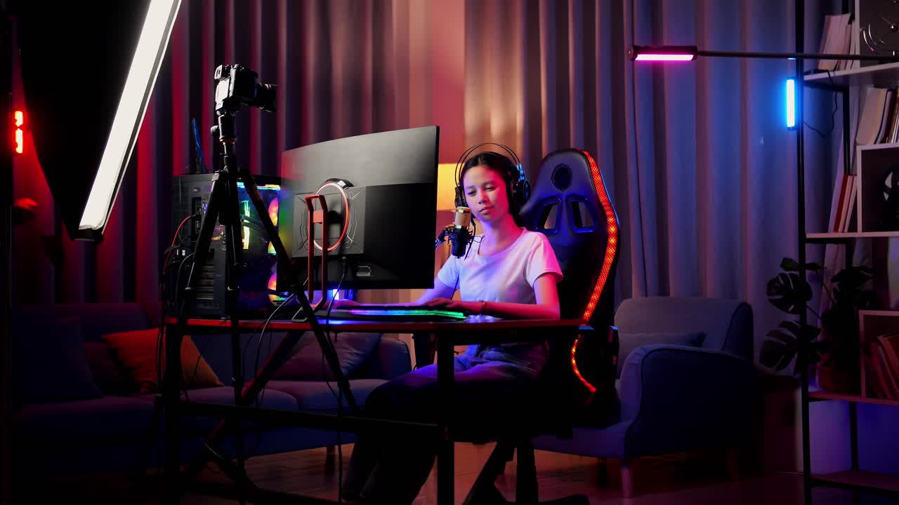 chica asiática que se estira mientras juega un juego a través de la red en una computadora personal. videojuego de transmisión en vivo, escritorio iluminado por luz de tira led rgb