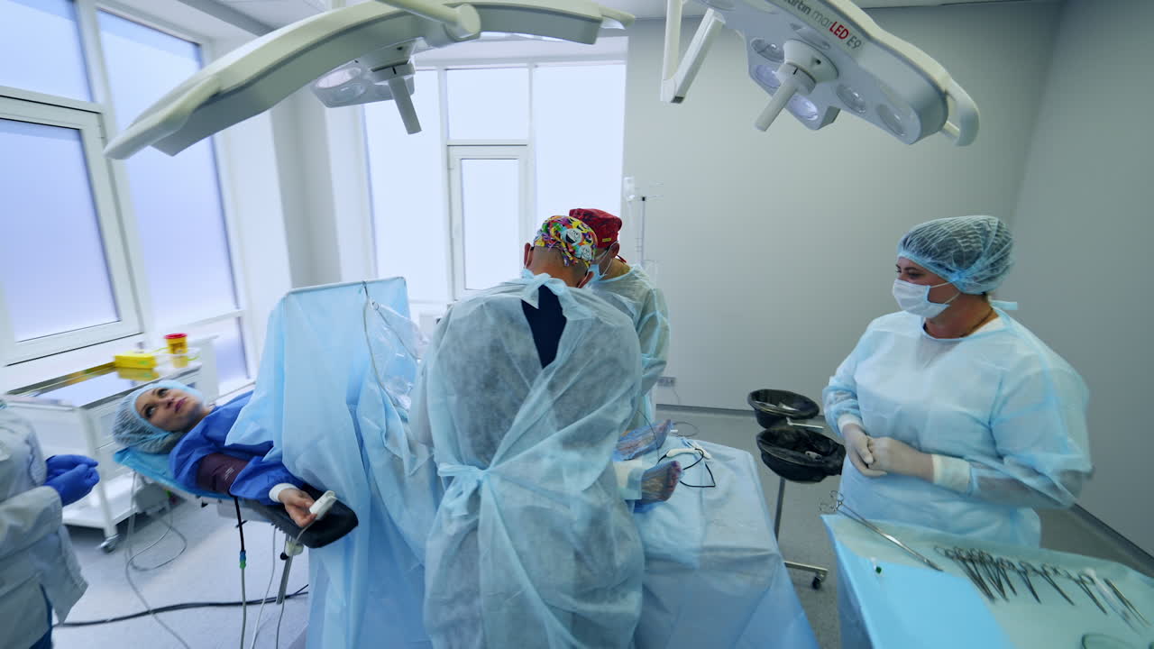 Team of surgeons performing the vascular operation in modern light room. Patient in consciousness talking to a nurse. Circle footage.